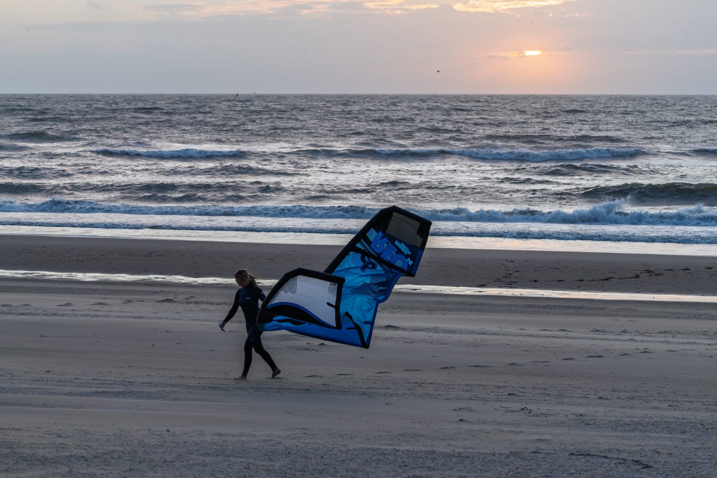 Wing foiler walks the dusk shoreline