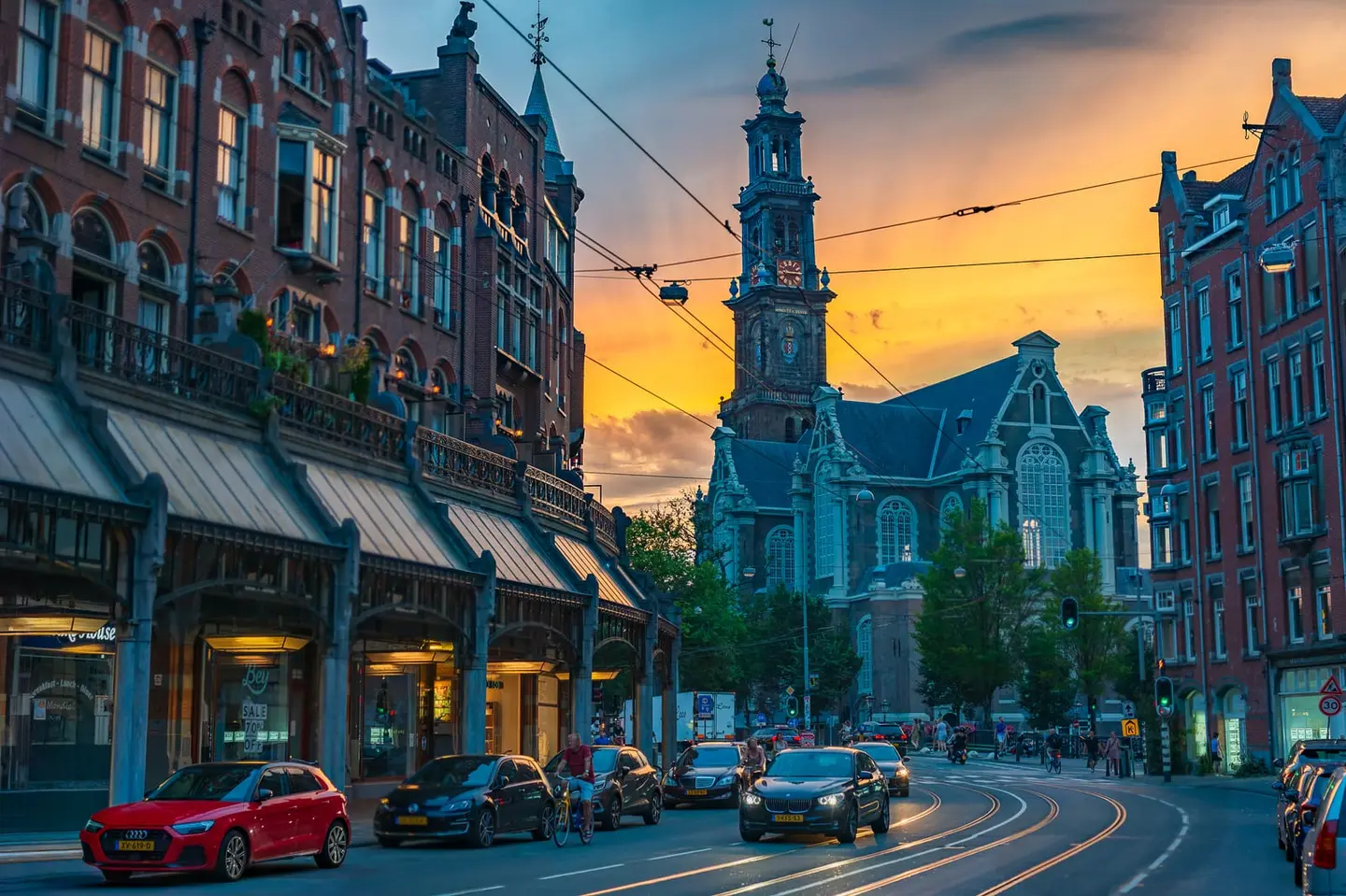 Evening traffic streams down Raadhuisstraat as a fiery sunset burns behind the tower of the Westerkerk in Amsterdam's historic centre.